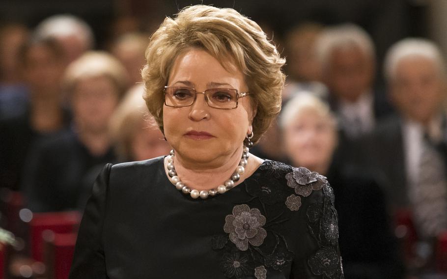 A woman with a somber expression and a pearl necklace.