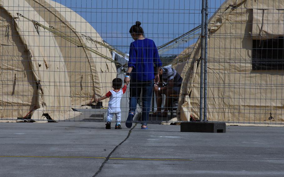 A woman takes the hand of a child behind a fence that surrounds temporary living facilities for Afghan evacuees at Ramstein Air Base, Germany, Aug. 21, 2021.