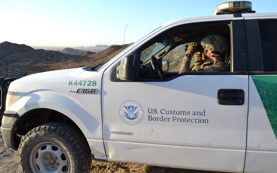 A soldier sits in a truck looking out with binoculars.
