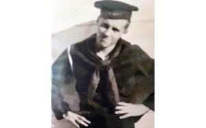 A black-and-white, 1940s-era portrait of a Navy sailor in hat and uniform posing with his hands on his hips.