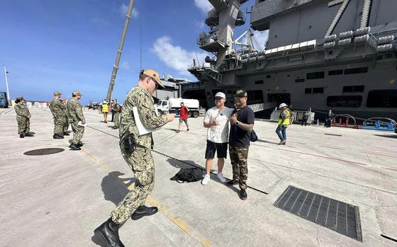Sailors pose with the USS Theodore Roosevelt after the San Diego-based aircraft carrier arrived at Naval Base Guam, Tuesday, Feb. 6, 2024. 