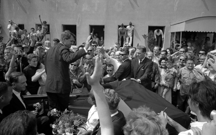 RFK waves a hand while standing in a car, as fans around him wave back.