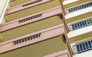 Mulitple floors of balconies, seen from below, on the outside of a military housing complex, two of which have damaged concrete on the underside.