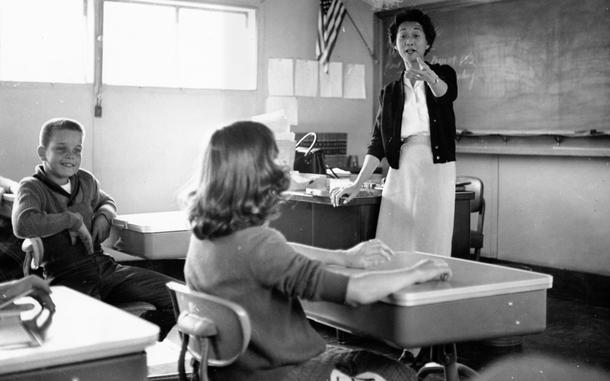 A black and white photo of children and a teacher in a classroom.