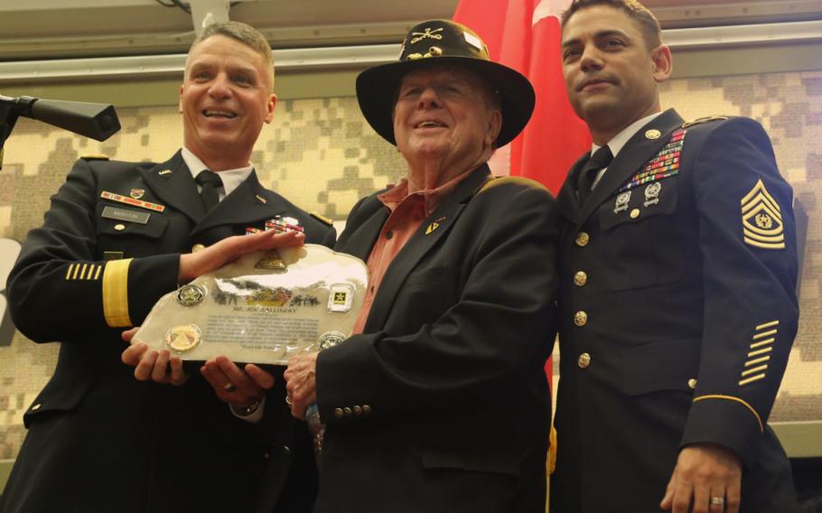 National Training Center Command Team, Maj. Gen. Joseph M. Martin and Command Sgt. Maj. Edison M. Rebuck present a gift to Joseph Galloway. Galloway was recognized with the Bronze Star with Valor when during the November 1965 Battle of Ia Drang, he repeatedly disregarded his own safety to rescue wounded soldiers under fire. 