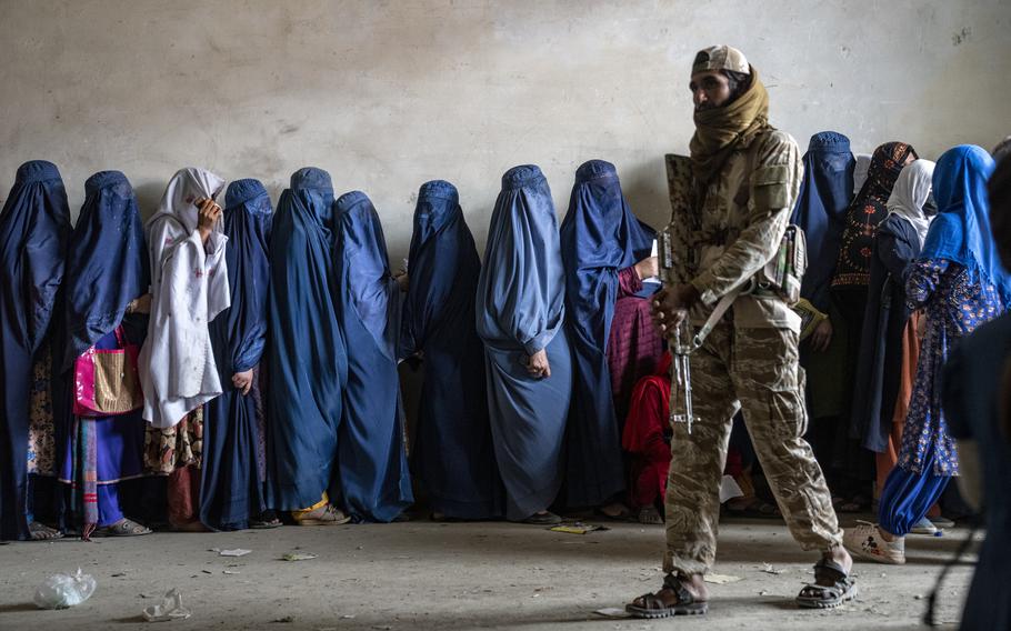 A Taliban fighter stands guard as women wait to receive food rations distributed by a humanitarian aid group, in Kabul, Afghanistan, Tuesday, May 23, 2023.  Two top international rights groups on Friday, May 26, slammed the severe restrictions imposed on women and girls by the Taliban in Afghanistan, saying they amount to the “crime against humanity of gender persecution.”