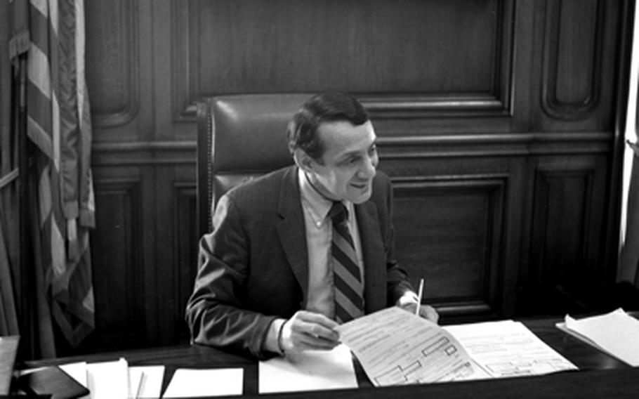 Harvey Milk sits at a desk going through paperwork.