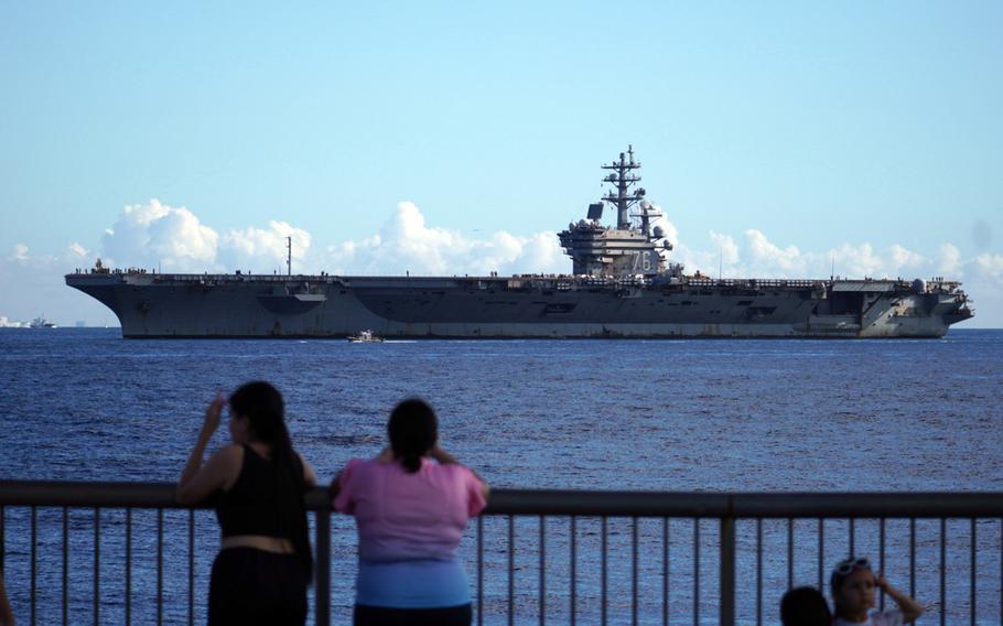 Family members gather along the base shoreline to watch the aircraft carrier USS Ronald Reagan return to Yokosuka Naval Base, Japan, Friday, Aug. 25, 2023.