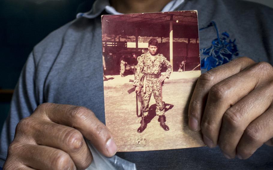 Reginaldo Cuxum Gomez, 42, shows a photo of his father, Francisco, wearing his uniform. On the back of the photo is written "in memory of the military zone of Coban" in Rabinal, Guatemala, on Feb 2, 2022. 