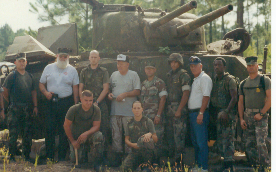 A group of people take a photo with a tank.
