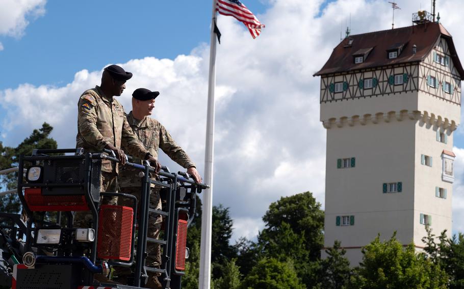 Outgoing commander Col. Christopher R. Danbeck, right, and incoming commander of U.S. Army Garrison Bavaria, Col. Kevin A. Poole, overlook a change of command ceremony at Tower Barracks, Grafenwoehr, Germany, July 12, 2022. The ladder truck lift symbolizes the current commander showing the incoming commander all of his responsibilities. 