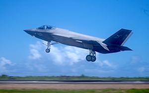 A military fighter jet lands on a runway with clouds and the horizon in the background.