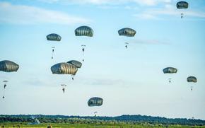 Ten U.S. soldiers parachute into a green field as others look on from the ground.