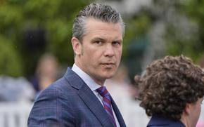 Pete Hegseth, viewed from the side, wears a dark blue suit with red plaid stripes.