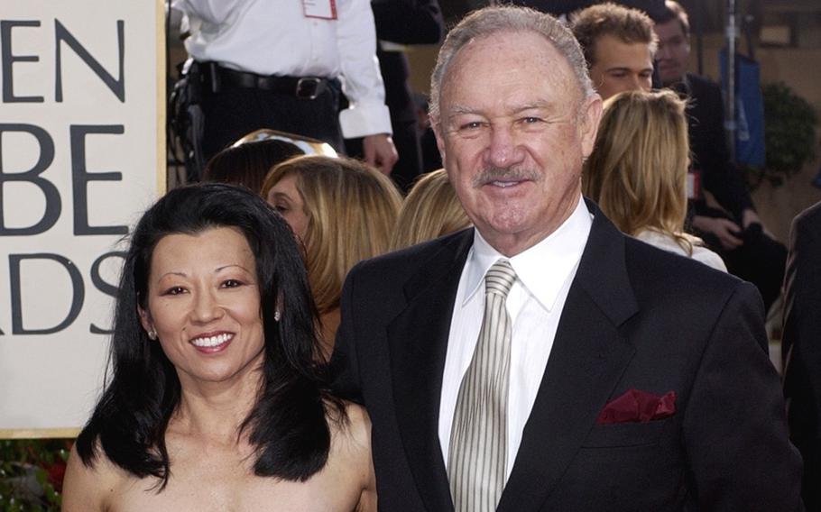 Gene Hackman, wearing a dark suit and white shirt, poses with his wife Betsy Arakawa on the red carpet at an awards show.