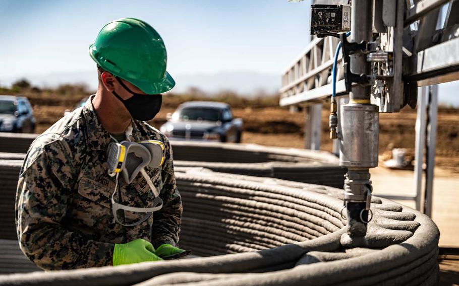 A service member examines a 3D printing machine being used to build a structure to hide military vehicles at Camp Pendleton, Calif. 