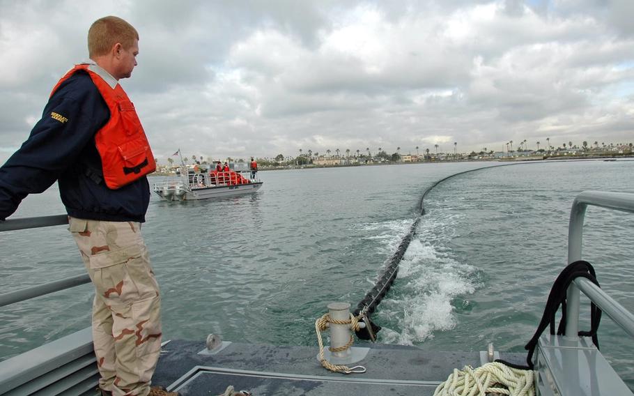 Naval Weapons Station Seal Beach training and readiness officer Allan Roy monitors the deployment of an oil containment boom during oil spill response training in Anaheim Bay. 
