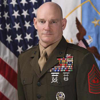 Official military portrait of a Marine officer in dress uniform standing in front of a U.S. flag.