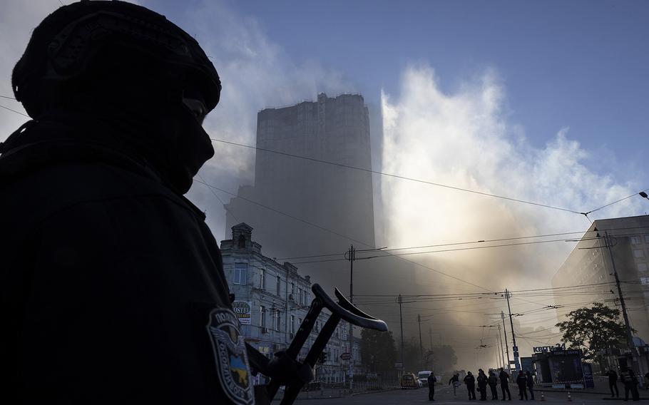 A member of the Ukrainian police force stands guard next to smoke as Kyiv is rocked by explosions during a drone attack in the early morning on Oct. 17, 2022, in Kyiv, Ukraine. The explosions, which authorities reported were caused by “kamikaze drones,” came a week after Russian missile strikes hit across Ukraine. 