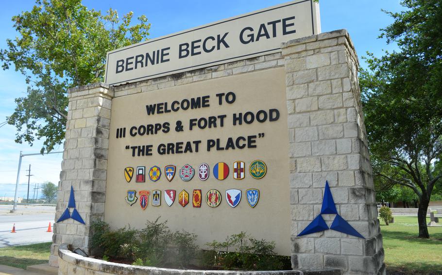 A stone sign outside the entrance to a military base reads “Bernie Beck Gate Welcome to III Corps & Fort Hood ‘The Great Place’ “ with trees behind it.