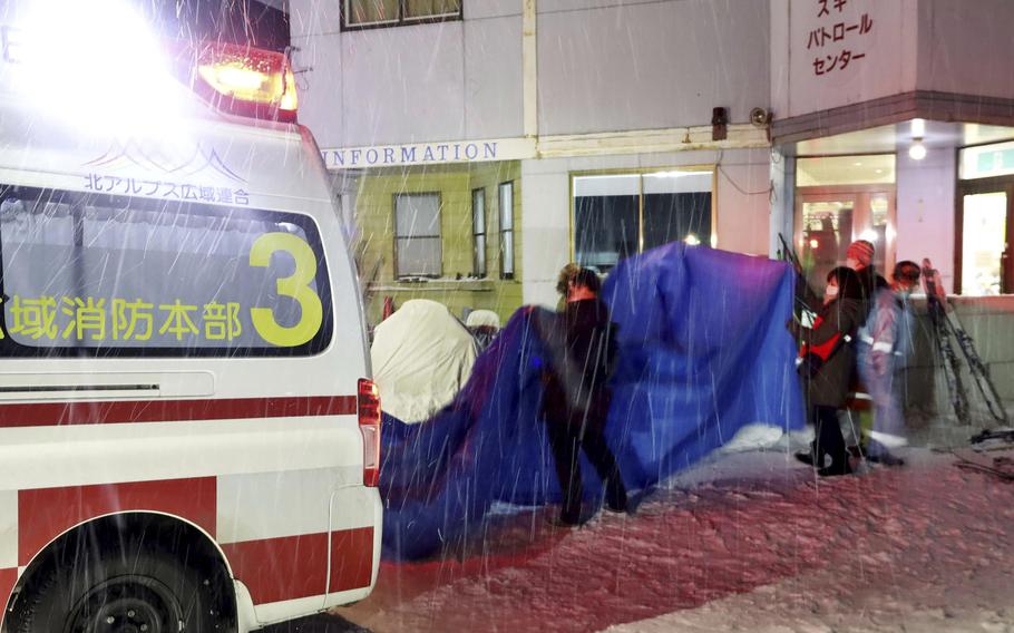 Injured skiers, behind a blue sheet, get into an ambulance at a ski resort in the village of Otari, Nagano prefecture, Japan, Sunday, Jan. 29, 2023. 