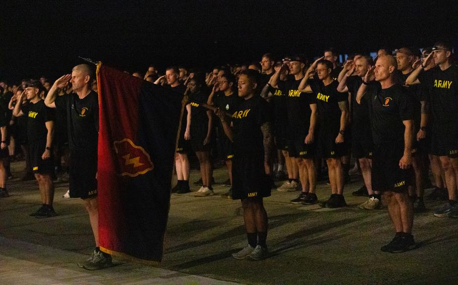 Rows of soldiers in black shirts and shorts saluting in formation.