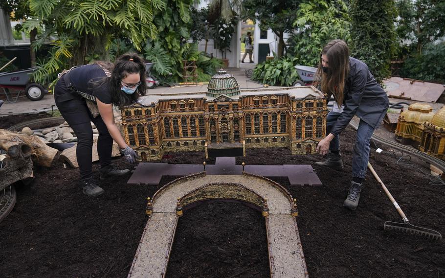 Laura Busse Dolan, right, and Annie Gessendorf carefully place the newest creation in the Holiday Train Show, a miniature of the LuEsther T. Mertz Library, in a bed at the New York Botanical Garden in New York, Thursday, Nov. 11, 2021. The show, which opens to the public next weekend, features model trains running through and around New York landmarks, recreated in miniature with natural materials. 