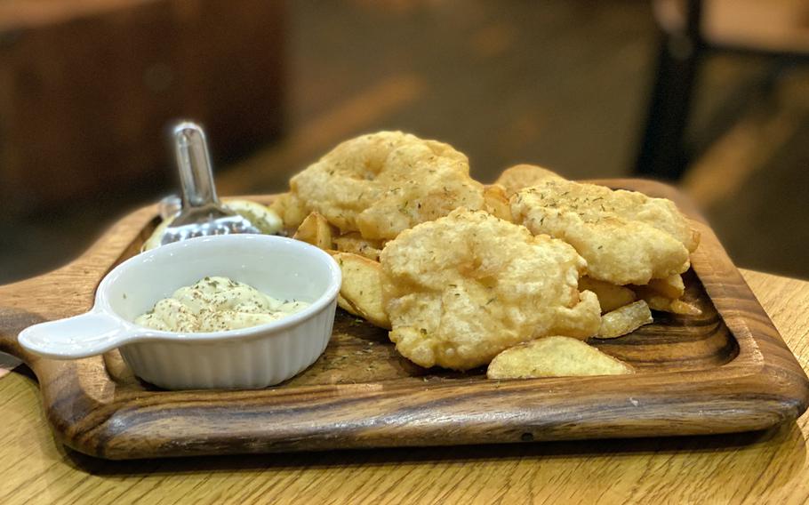 Fish and chips and a side of tartar sauce on a wooden platter.