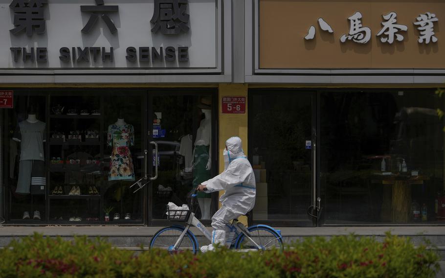 A worker in a protective suit rides a bicycle past shuttered retail shops after authorities ordered the closing down of non-essential businesses and asked people to work at home in the Chaoyang district on Monday, May 9, 2022, in Beijing. 