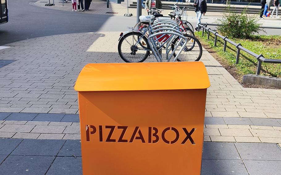An orange metal trash container with the word “PIZZABOX” engraved on it.
