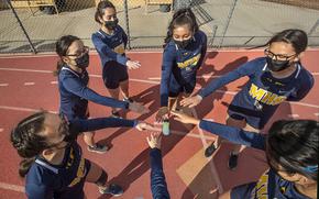 Members of the Montebello High School girls cross country team are careful not to touch hands while wearing masks as they huddle up before a home meet against Bell Gardens High School. 