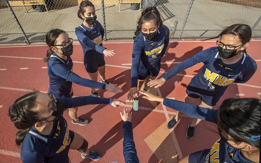 Members of the Montebello High School girls cross country team are careful not to touch hands while wearing masks as they huddle up before a home meet against Bell Gardens High School. 
