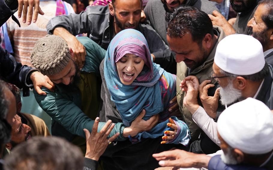 A woman in a headscarf, seen from above, cries aloud while surrounded by other mourners at a funeral.