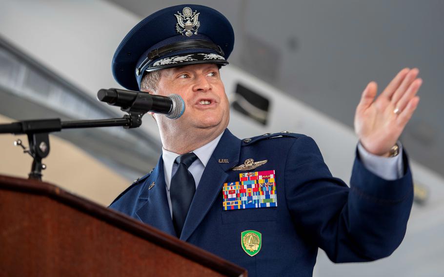 Phillip Stewart, in uniform and wearing a hat, stands at a podium, speaking and gesturing with his left hand.