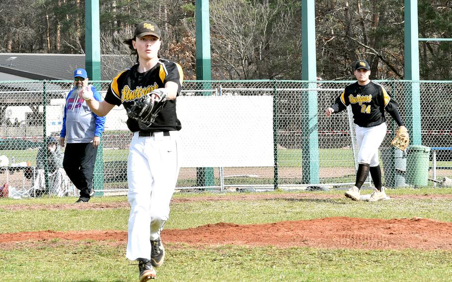 Der Stuttgarter Pitcher Jamie Arnold zeigt auf die erste Base, nachdem er im ersten Spiel eines Doubleheader-Samstags gegen die Royals auf dem Baseballfeld in der Nähe des Southside Fitness Centers auf der Ramstein Air Force Base in Deutschland einen Bodenball eingesetzt hat.  Im Hintergrund, von links nach rechts, sind Ramstein-Trainer Alfredo Rios und Panther-Drittbasisspieler Ryan Santana.