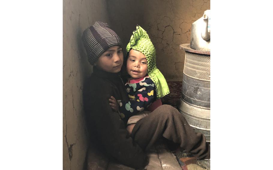 Beside a cold stove in their frigid two-room house in Kabul, a son of Mahmad Ewaz, a rural war refugee, tries to comfort his baby sister and keep her warm in Kabul, Afghanistan, on Jan. 3, 2022. 