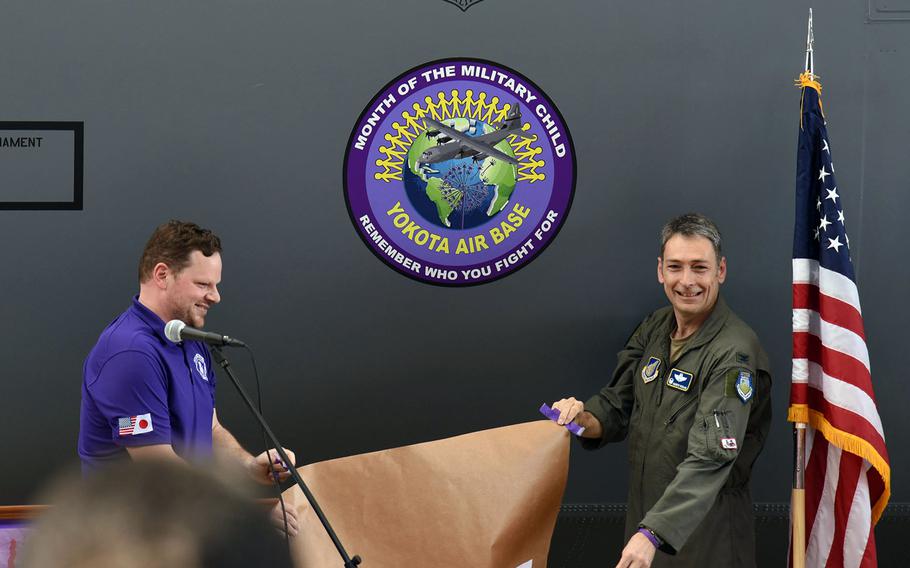 Joshua Fly, the school liason program manager, and Col. Andrew Roddan, commander of the 374th Airlift Wing, unveil the Month of the Military Child morale patch at Yokota Air Base, Japan, Tuesday, April 11, 2023.