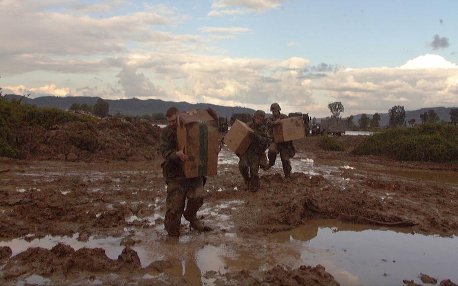 Spc. Daryl Dusharm, Spc. Geoffrey Johnson and Jacob Ainsworth carry supplies through the mud that surrounds Task Force Hawk base camp in Tirana, Albania, April 19, 1999.