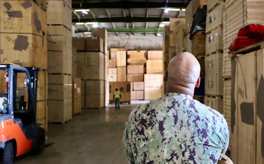 A sailor, back to the camera, scans boxes and boxes of troops’ possessions in a warehouse.