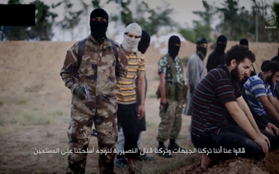 A still from an Islamic State propaganda video that Mohammed Khalifa narrated and appears in. Khalifa, front, is shown in the black mask and camouflage uniform, just before he shoots a kneeling Syrian soldier, left, execution-style, in the back of the head