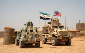 A tank flying a Syrian flag idles beside a tank flying an American flag.