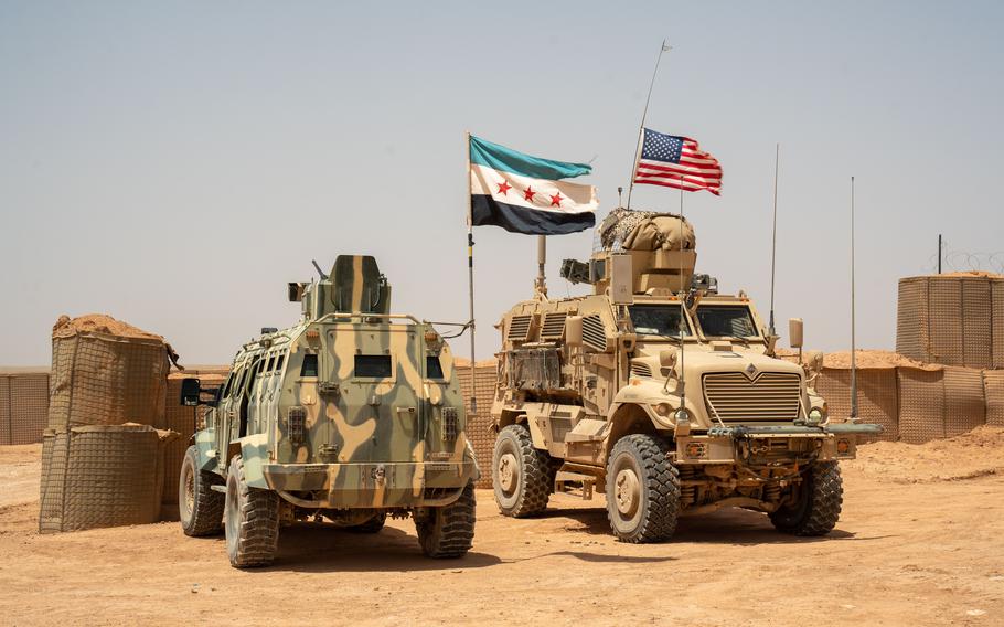 A tank flying a Syrian flag idles beside a tank flying an American flag.