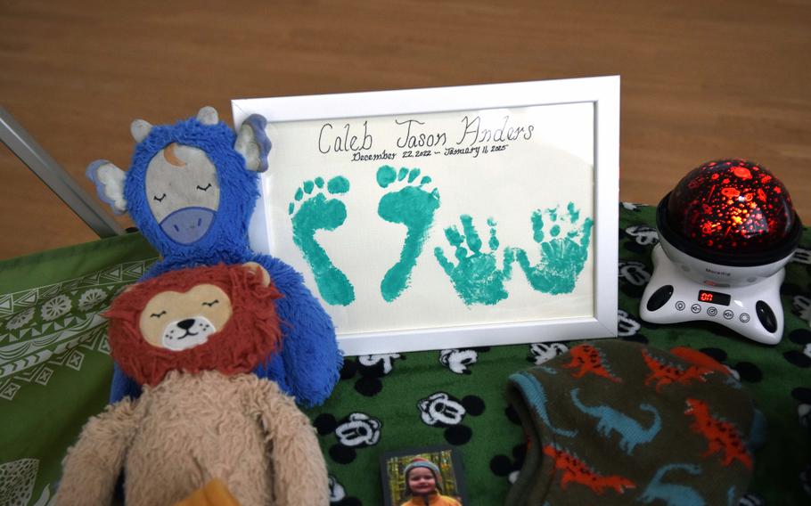 A plush lion, a stuffed cow and a nightlight sit alongside a frame with teal footprints and handprints in a frame reading “Caleb Jason Anders Dec. 22, 2022-Jan. 11, 2025.
