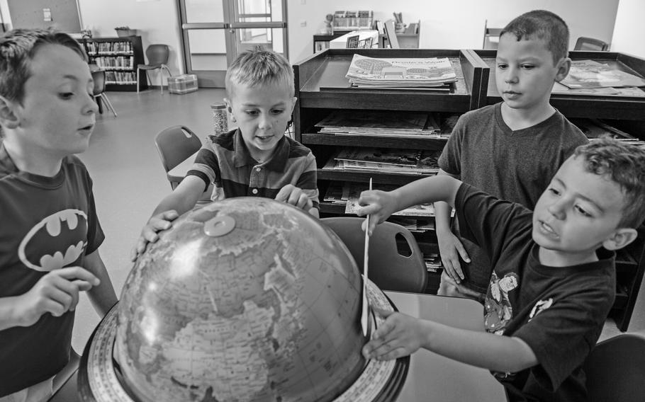 Four kids play with a globe in a classroom