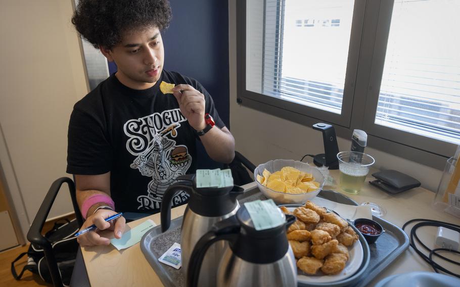 A man brings a chicken nugget to his mouth. In front of him is a platter of food and pots of coffee.