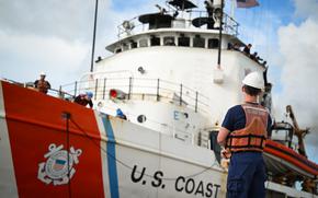 A Coast Guard member stands on the pier as the cutter sails in.