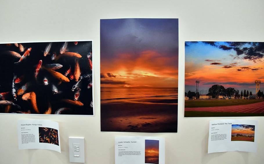 Photos of colorful koi in dark water, a golden sunset on a beach and a sunset photographed from Yokota Air Base’s track are displayed on a cream colored wall.