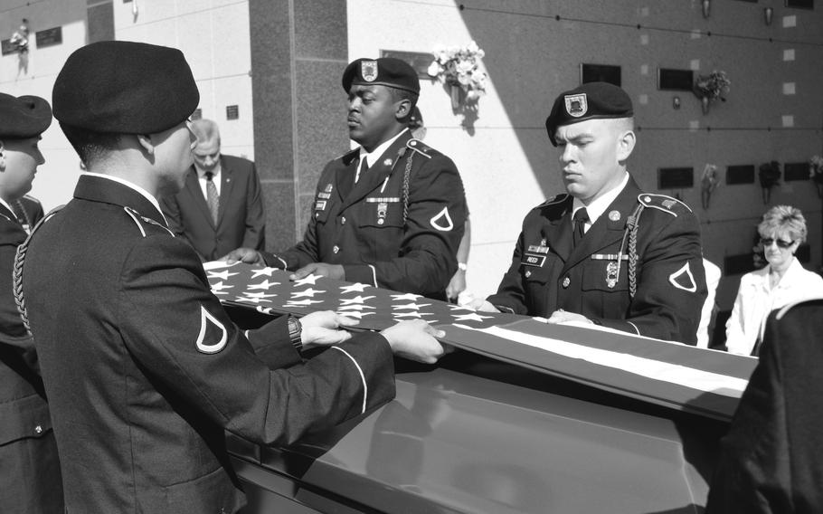 A black and white photo of an honor guard folding an American flag over a casket.