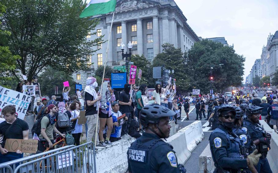 A crowd of protestors gather along the parade route as police stand guard.