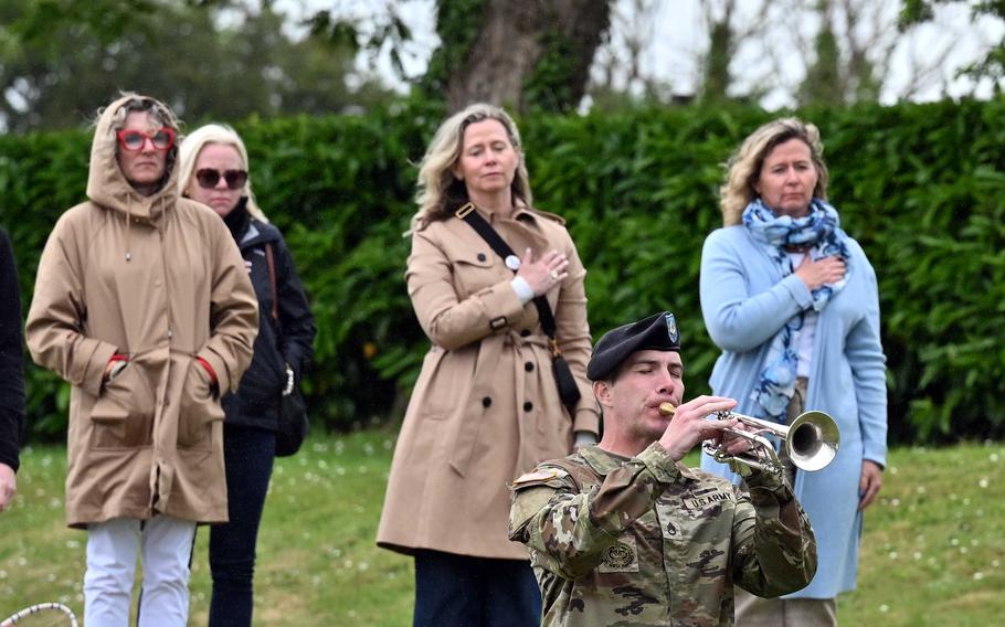A soldier plays a horn as civilians place their hands over their hearts.